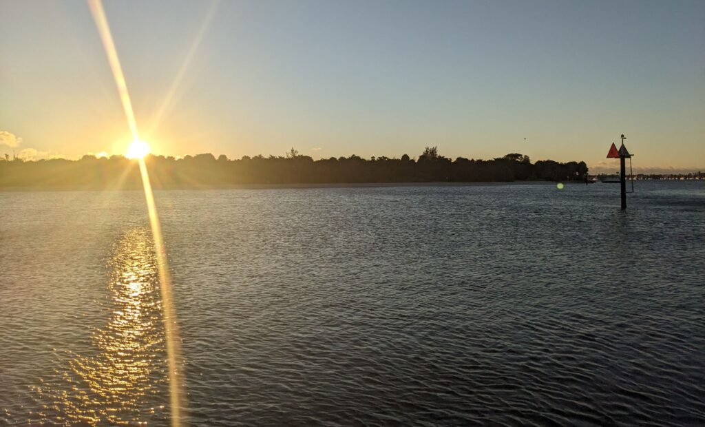 A sunrise over a small island with a red lateral marker '42' in the water.