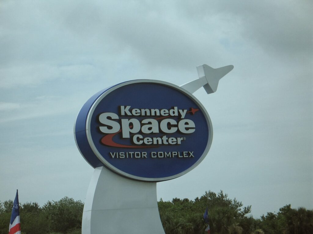 A sign for the Kennedy Space Center Visitor Complex in front of a cloudy sky.