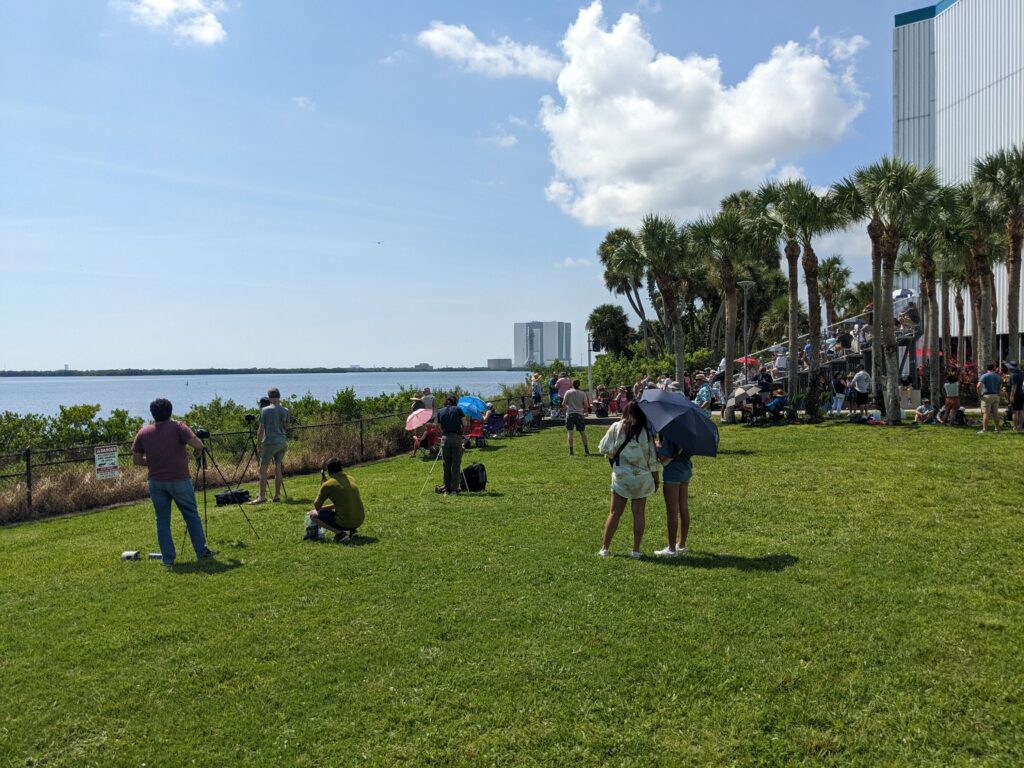 Some people standing on grass waiting for a rocket launch