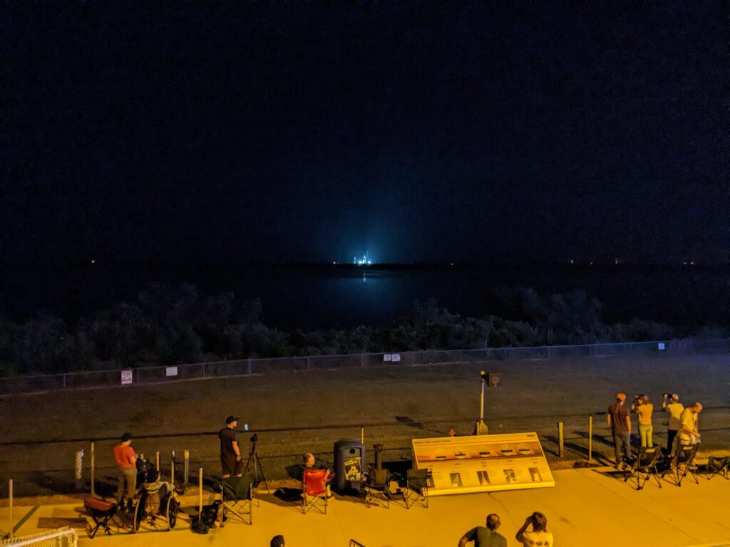 A rocket lit up in the distance at night as photographers set up