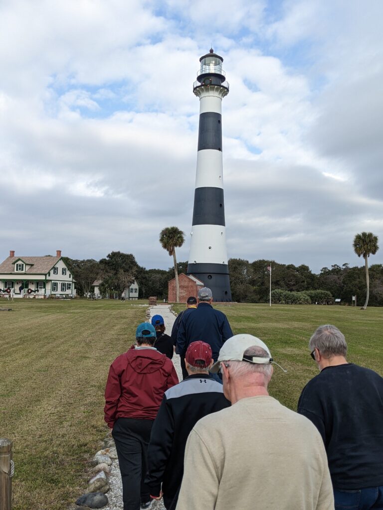 A group of people walking towards a black and white horizontally-striped lighthouse