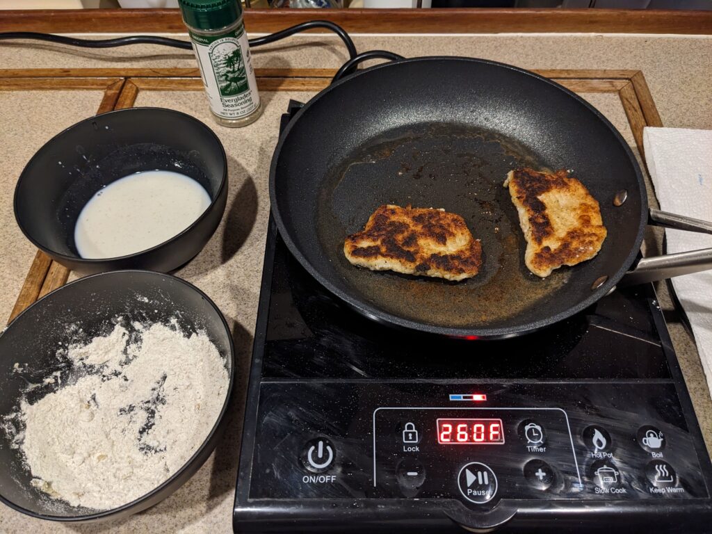 An electric hot plate with two lionfish fillets. Off to the side are the preparation ingredients.